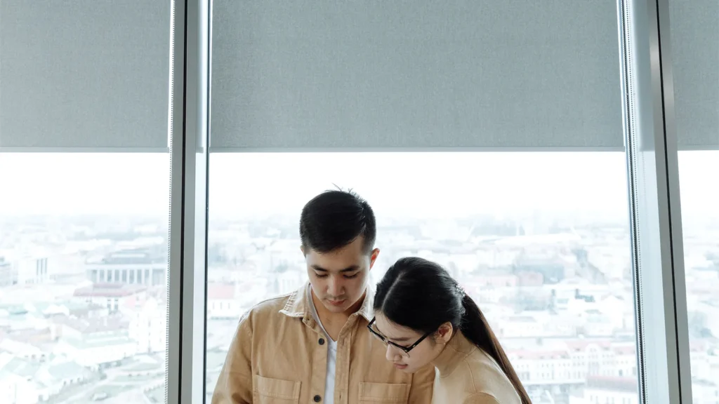 Two colleagues reviewing a document beside a large office window