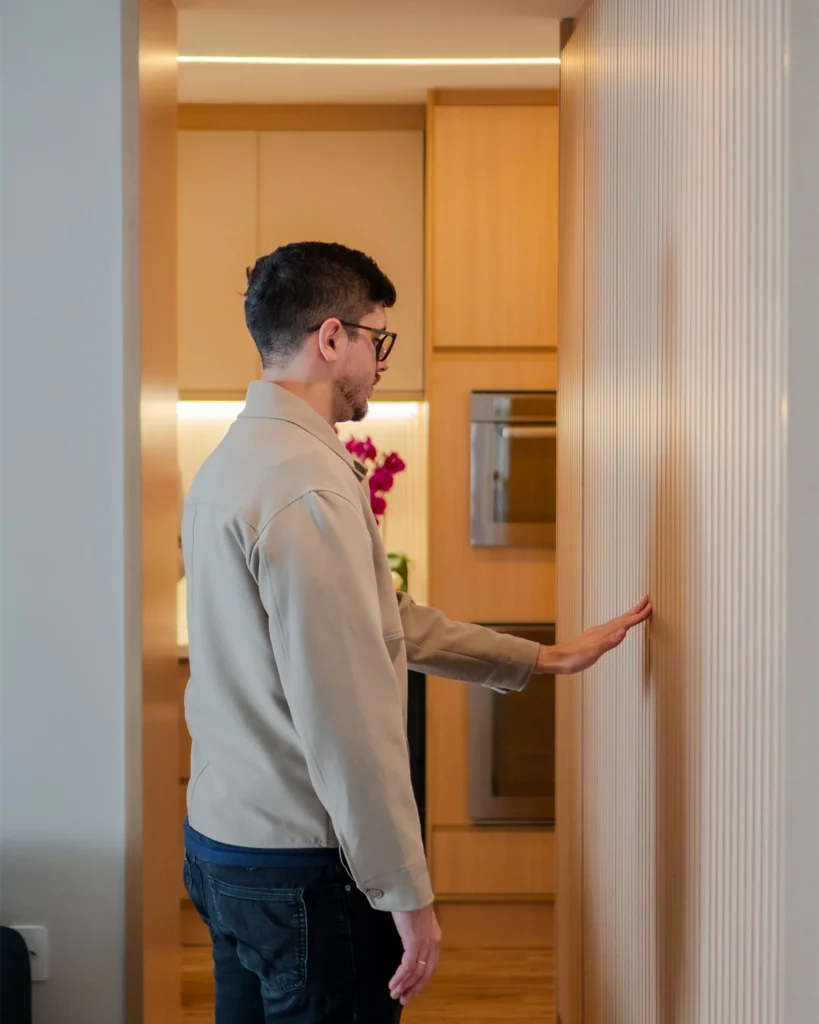 Man examining a wall panel and doorway inside a modern apartment