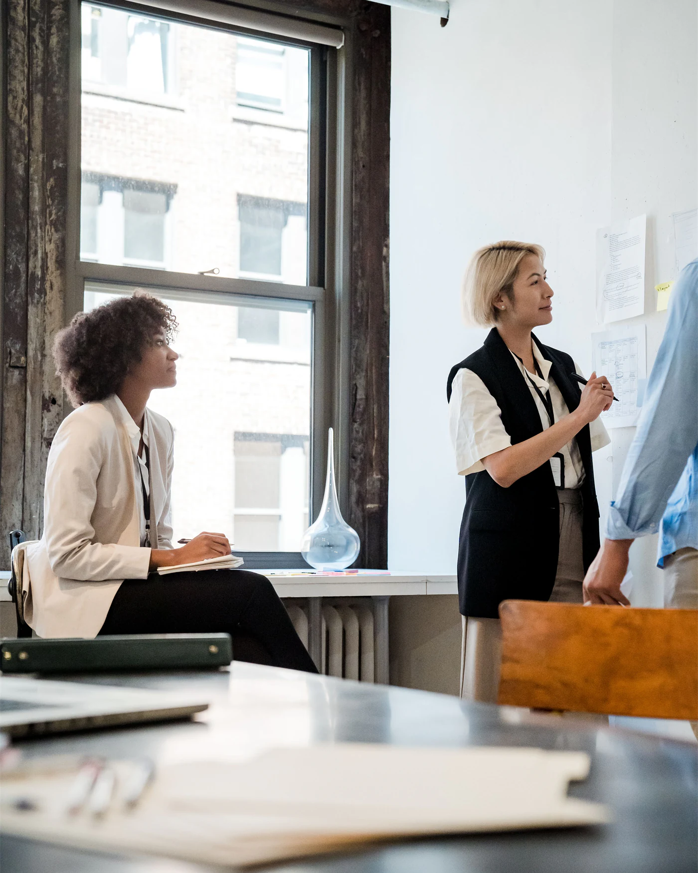 Two colleagues discussing work beside a window in a bright office