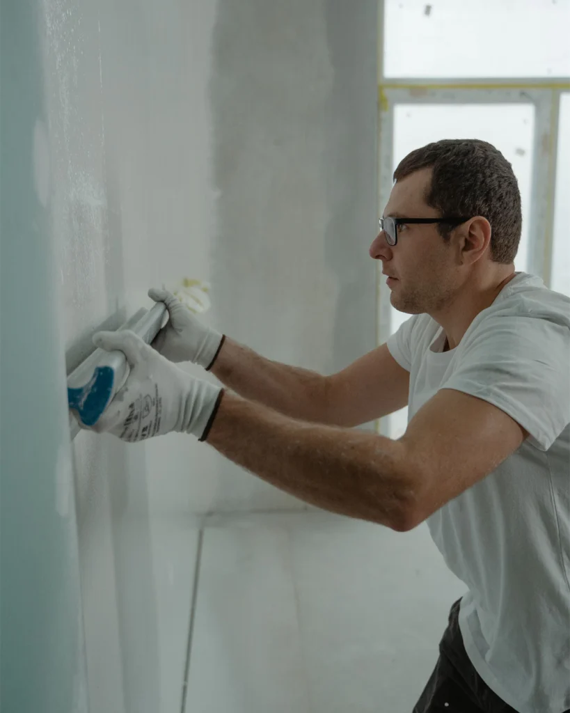 Tradesperson smoothing and repairing a wall inside a home