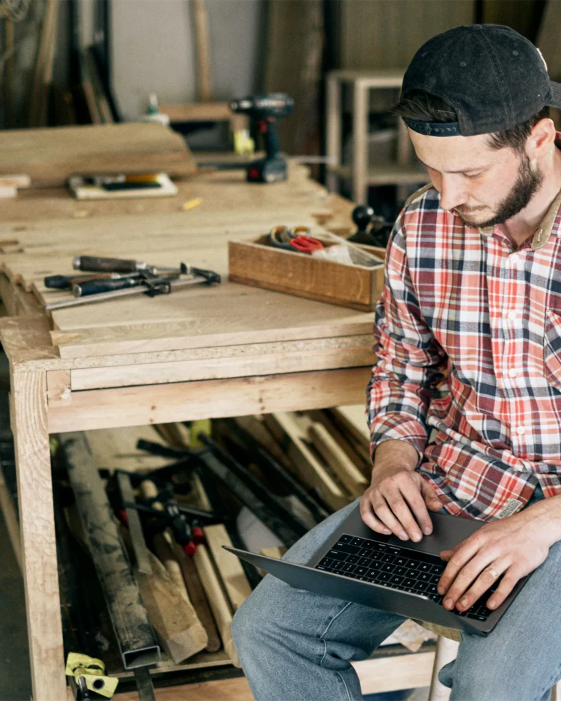 Small business owner working on a laptop in their woodworking workshop