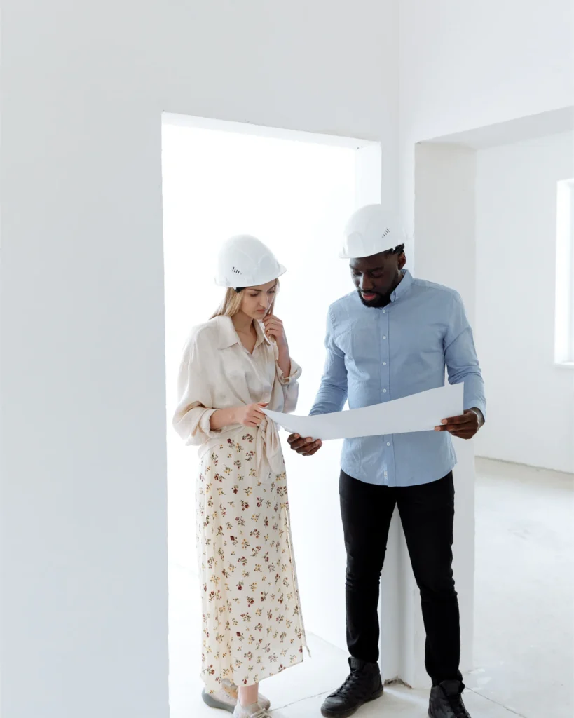 Two professionals reviewing building plans inside a property under construction