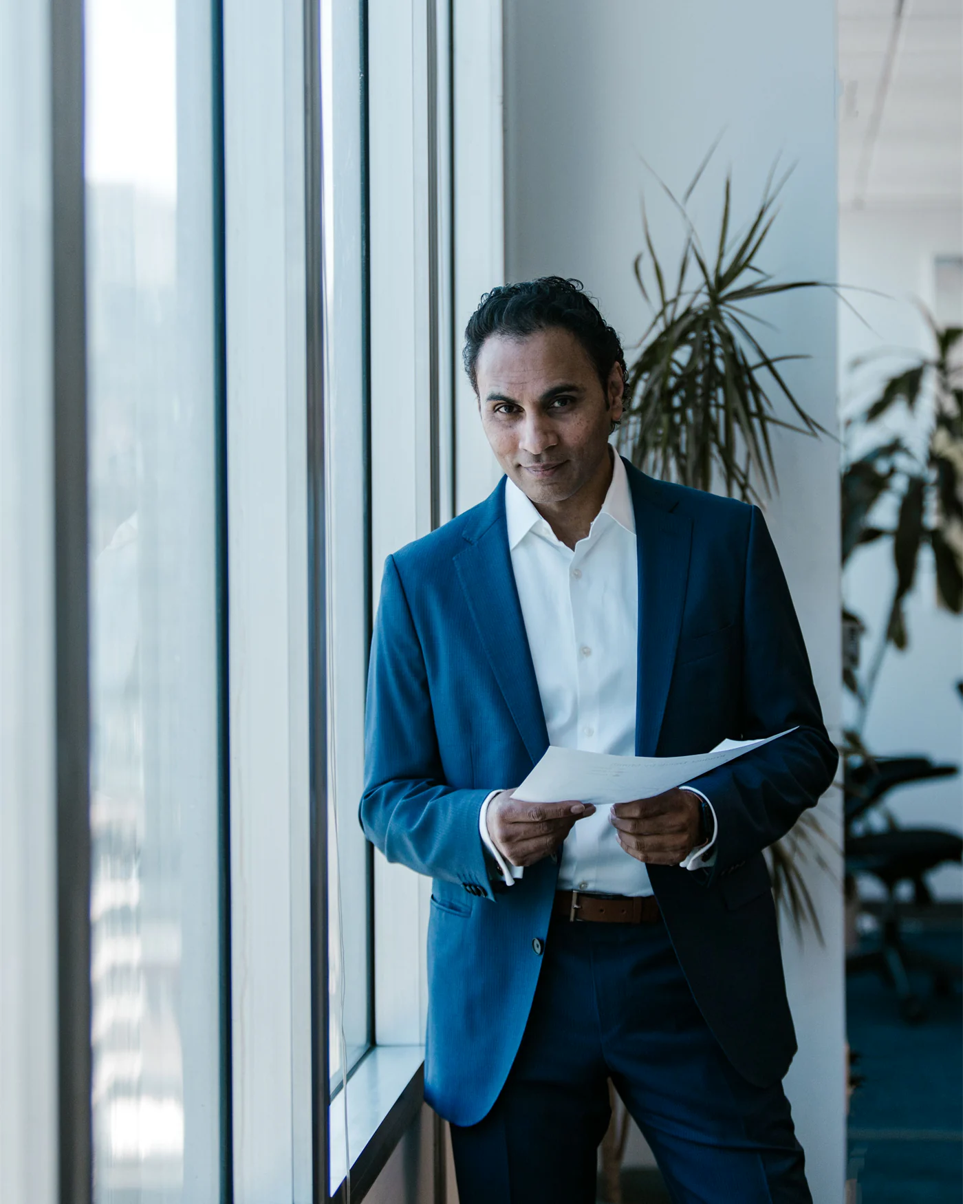 Executive standing with a document beside a large office window