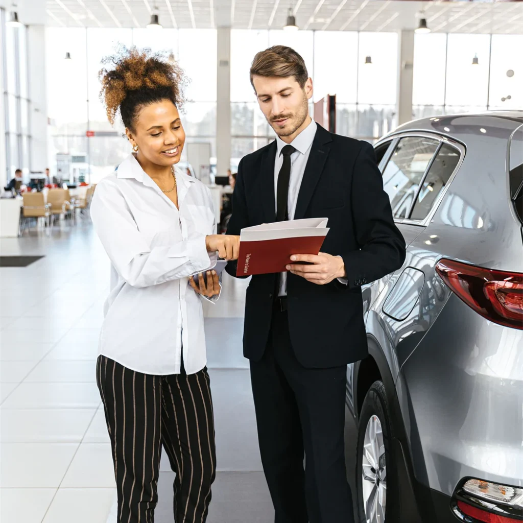 A representative going through documents with a client beside a vehicle