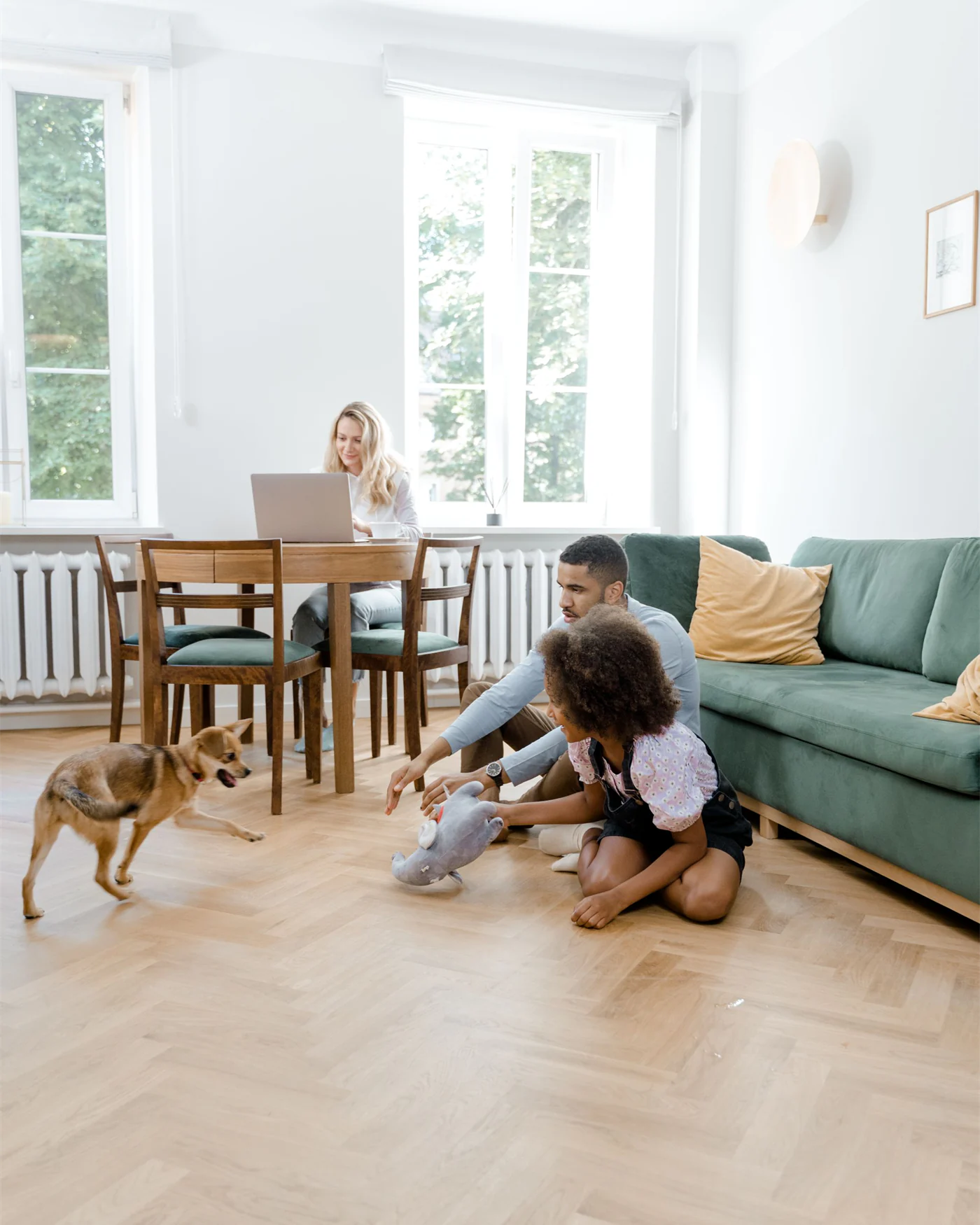 A bright Scandinavian apartment with a woman working at a table and a parent and child on the floor nearby