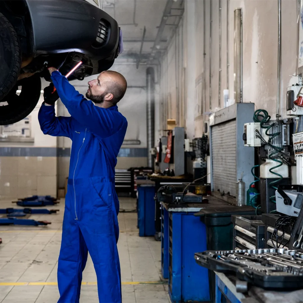 A mechanic examining the underside of a car raised on a workshop lift