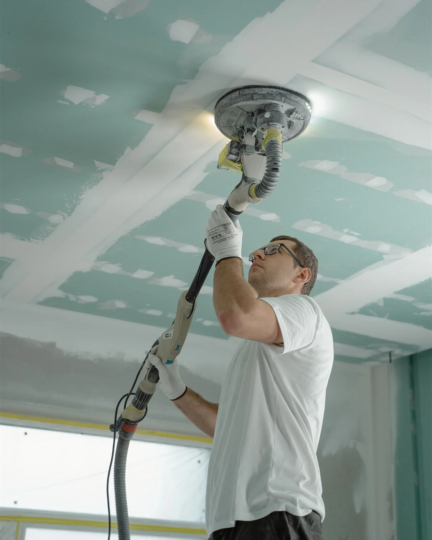 radesperson sanding a plasterboard ceiling during finishing work