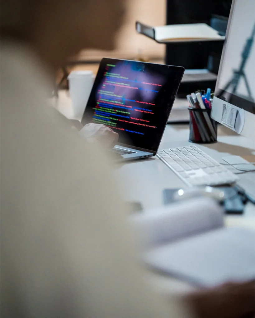 A laptop running code on a desk, shot through a shallow foreground
