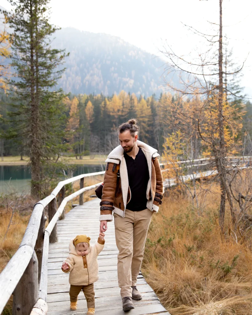 A father and young child walking together on a boardwalk in autumn